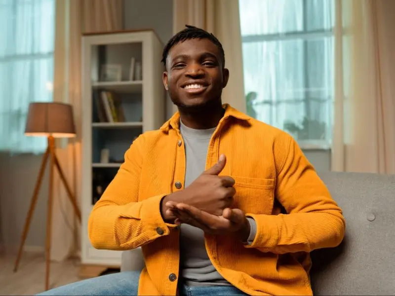 Homem sentado em um sofá fazendo um sinal de cumprimento na língua universal de sinais