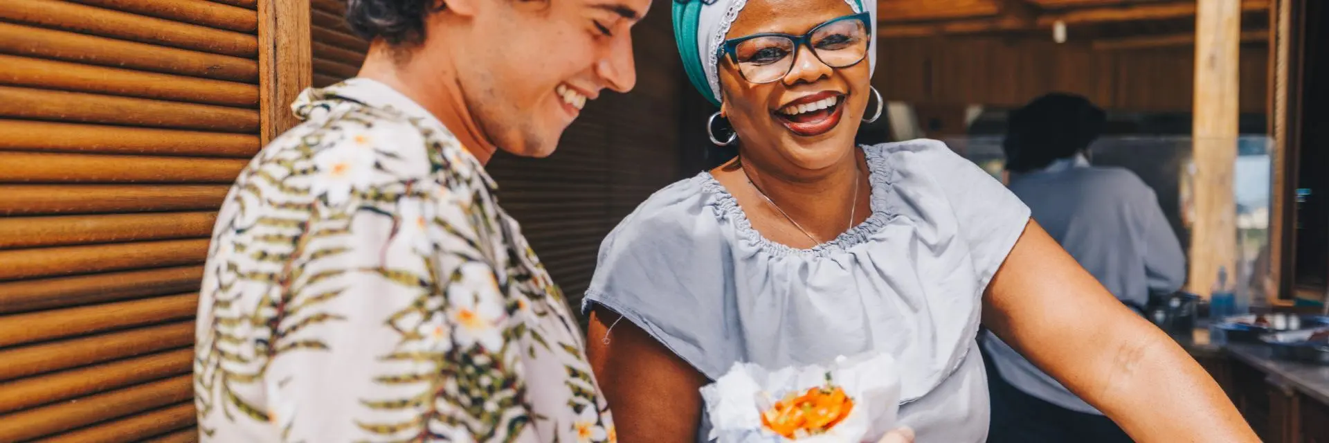 Mulher usando trajes de baiana e um homem sorrindo enquanto segura um acarajé