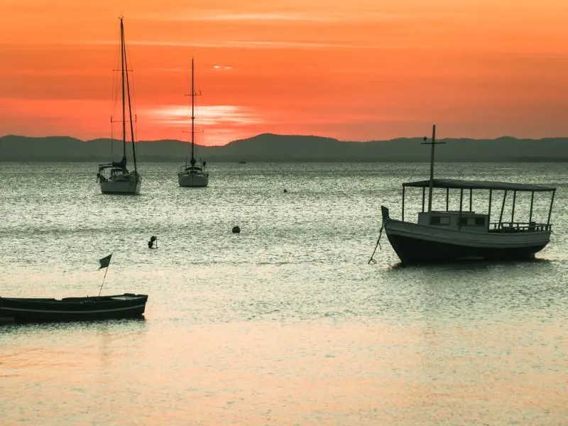 barcos ancorados proximos à praia de itaparica, com o pôr-do-sol no horizonte