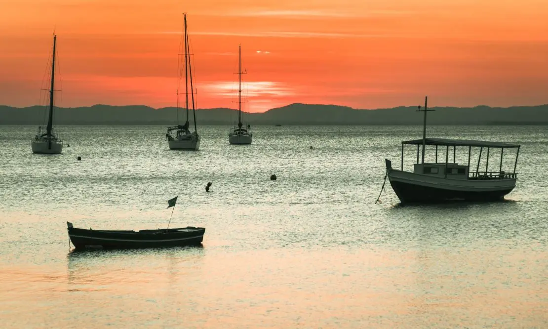 barcos ancorados proximos à praia de itaparica, com o pôr-do-sol no horizonte