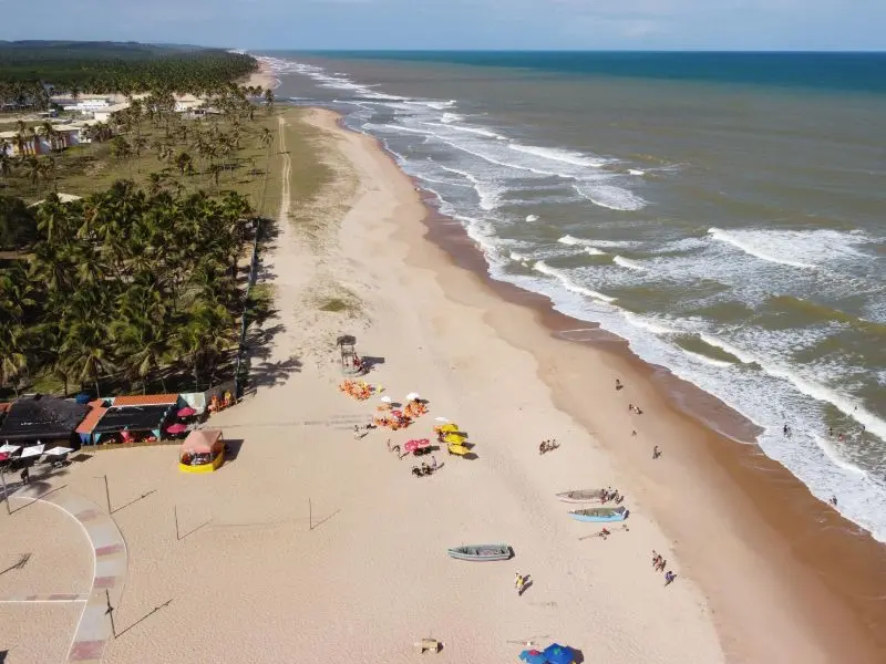 Vista aérea da orla da Praia de Baixio com pessoas, quiosques e caiaques parados na areia