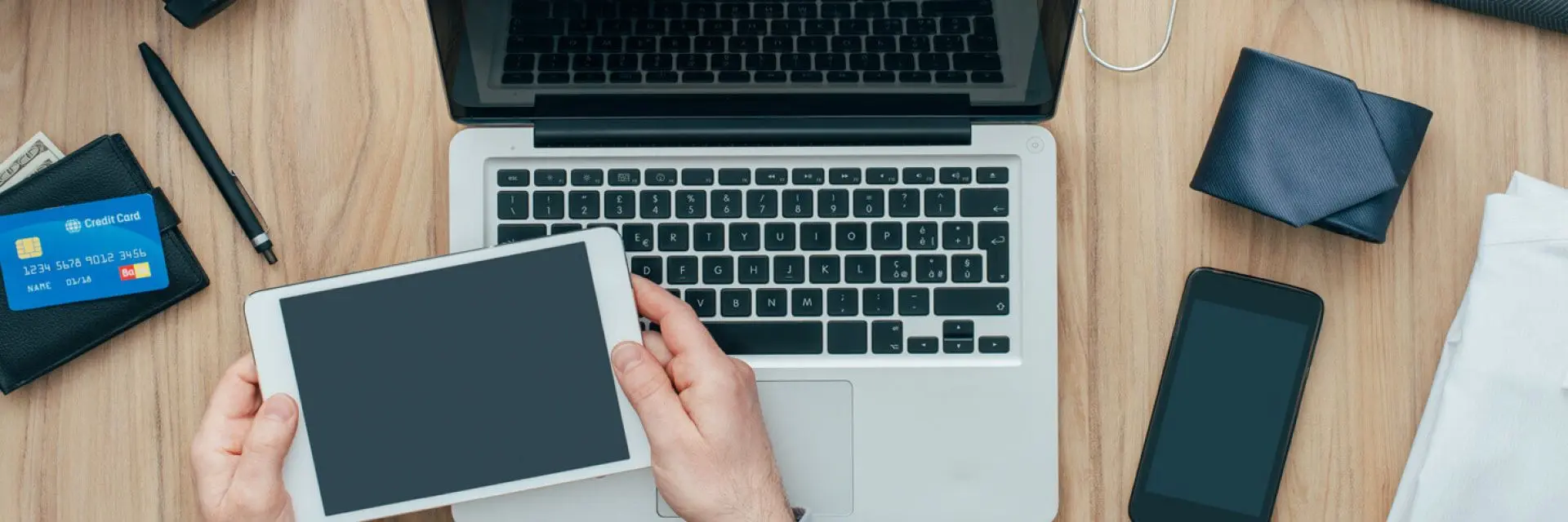 Imagem de uma pessoa segurando um tablet próximo de um computador e celular