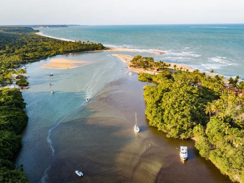 Orla da praia de Porto Seguro, com pequenos barcos entrando no rio que deságua no mar