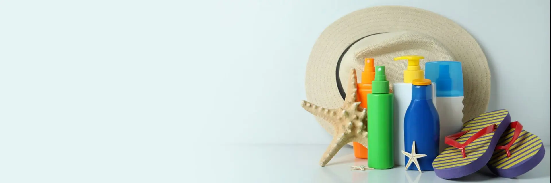 Imagem de um chapéu, protetores solar e chinelo num fundo azul.