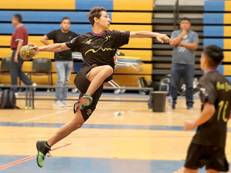 jogador em quadra arremessando bola de handebol