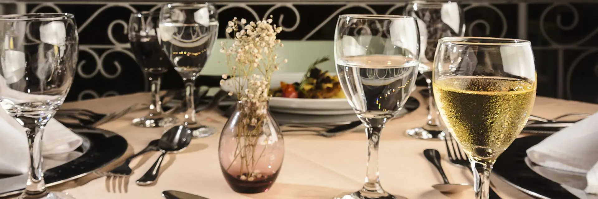 Imagem de uma mesa posta. Nela é possível ver taças, pratos, talheres e enfeites para deixar a decoração mais bonita.