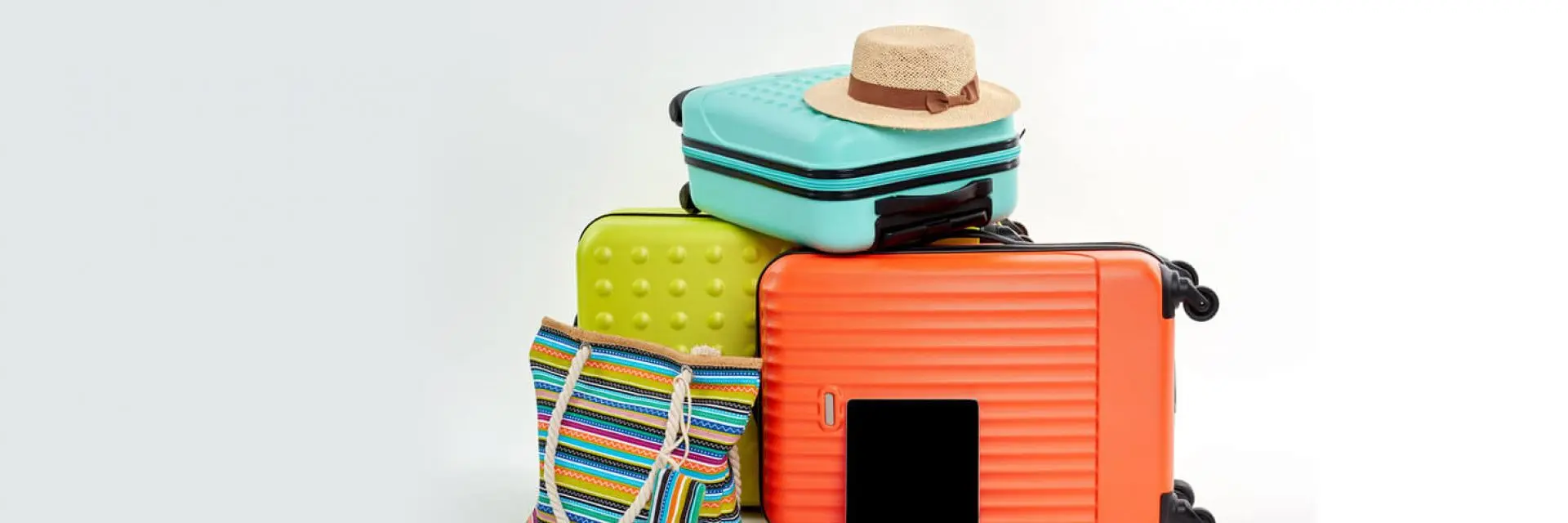Imagem de várias malas empilhadas. Um delas é listrada e colorida e as outras estão nas cores laranja, verde e azul.