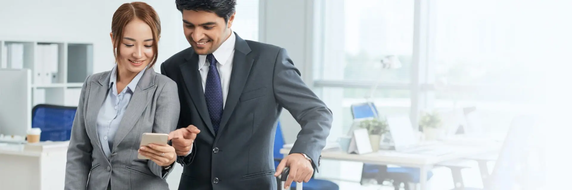 Imagem de duas pessoas se planejando para uma viagem corporativa. Ambas estão usando ternos e estão olhando um celular.